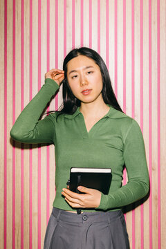 Woman holding notebook against striped pink and wood wall