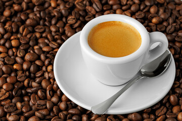 White espresso cup filled with rich coffee, resting on a bed of roasted beans, with spoon placed gently on its saucer, inviting moment of indulgence