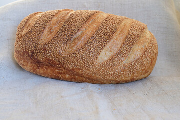 Sourdough loaf sprinkled with sesame seeds. Sesame white bread on a hemp coarse cloth. Copy space.