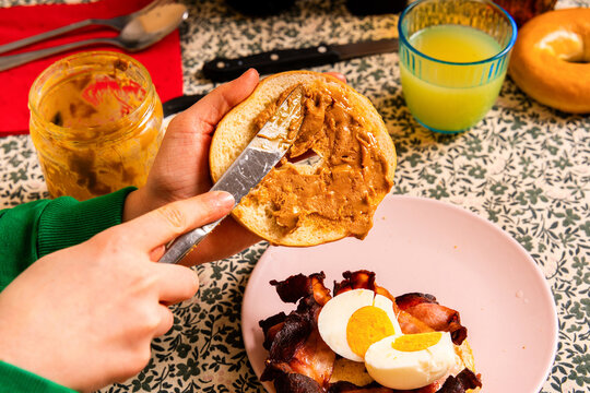 Spreading Peanut Butter on a Bagel with Bacon and Eggs

