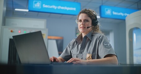 Airport Security Checkpoint: Female Security Officer in Headset Using Laptop, Looking at Camera....