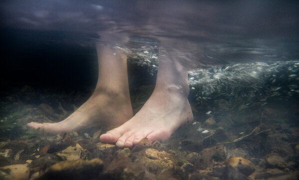 Bare white feet stand on rocky river bottom