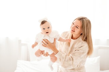 a mother with a newborn baby in her arms at home on a white background of a bed or window, a space for text, a young mother gently kisses and hugs her baby, maternal love