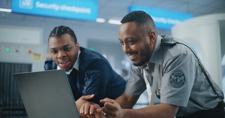 Airport Security Checkpoint: African American TSA Workers Using Laptop, Discussing Security Issues....