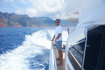 Deckhand standing barefoot on yacht deck with ocean waves and American flag