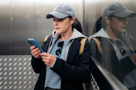Woman using smartphone while riding modern elevator