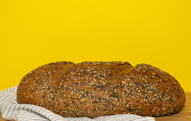 Artisanal wholemeal rye bread on a kitchen cloth and wooden board on a yellow background. Nutritious food with a high level of fiber