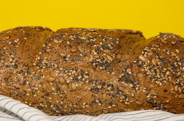Close up of artisan rye whole grain bread on a kitchen cloth and wooden board on a yellow background. Nutritious food with high fiber level