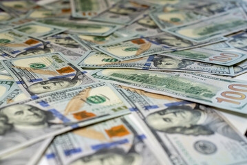 Stacks of hundred-dollar bills are spread out on a surface emphasizing the details of the new currency design side view in close up