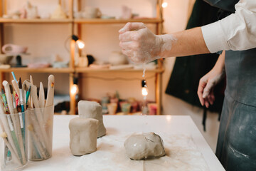 Craftswoman is preparing clay for making ceramic crockery. Female potter rolls piece of clay before...