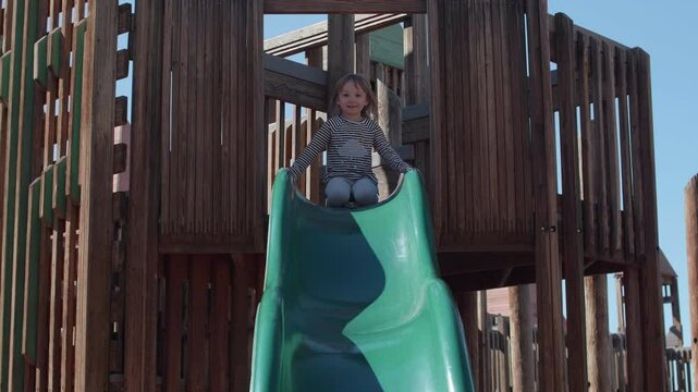 Little Toddler Girl Sliding down a green wooden playground Slide