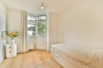 A serene bedroom showcasing minimalist design, featuring a bed, wooden flooring, and large windows that invite natural light, complemented by a vase of flowers.