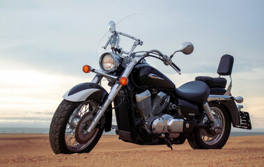 A lone motorcycle stands on the sandy surface of the Namib Desert against a dramatic cloudy sky....