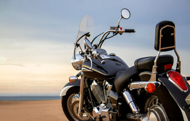 A lone motorcycle stands on the sandy surface of the Namib Desert against a dramatic cloudy sky. The sunset lighting highlights the contrast between nature and machine.