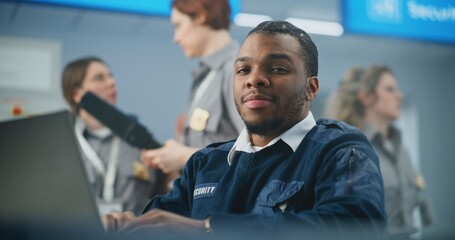 Airport Security Checkpoint: African American TSA Officer Using Laptop, Smiling and Looking at...