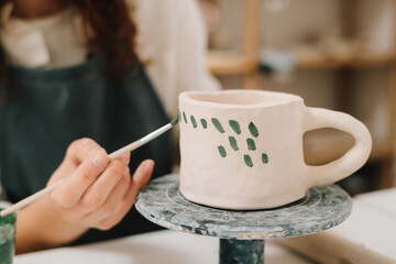 Artisan stamps decorative symbols on the dry clay of the cup. Process of designing cup with a traditional pattern.