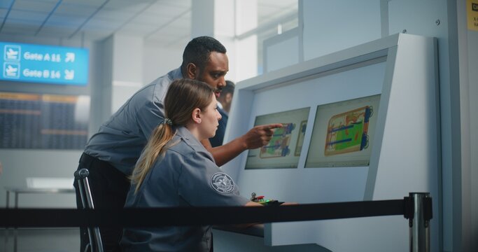 Airport Security Checkpoint: Two Multiethnic Security Officers Monitoring X-ray Images of Baggage Screening Procedure on Computer Screens Using Modern Software. Rack Focus on Baggage Restrictions Sign