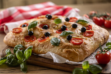 Focaccia - Italian Bread with tomatoes basil leaves olives and olive oil on cutting board