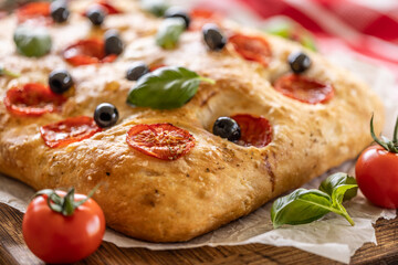 Focaccia - Italian Bread with tomatoes basil leaves olives and olive oil on cutting board