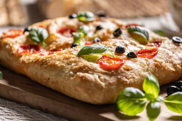 Focaccia - Italian Bread with tomatoes basil leaves olives and olive oil on cutting board