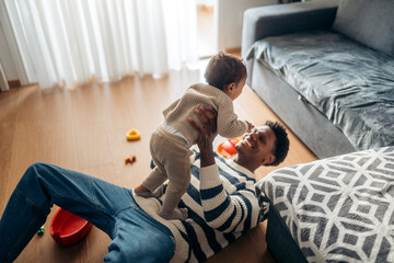 Happy father lifting baby son while playing together on the floor