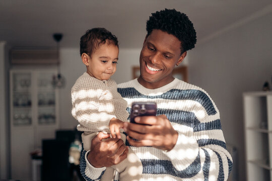 Father holding his baby while using smartphone at home
