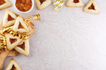 Close up freshly baked triangular cookies filled with fruit surrounded by golden decorations ribbon on a wooden cutting board. Purim celebration concept. top view. space for text