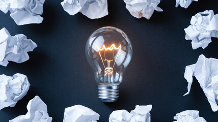 Glowing Light Bulb on a Dark Background with Crumpled Papers