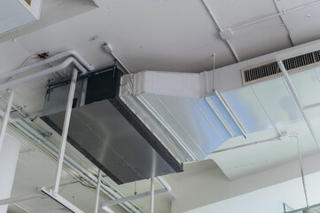 Modern air conditioning system installed in warehouse ceiling, featuring metal ducts, pipes, and...