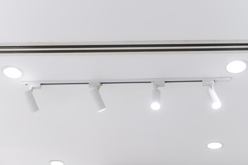 Modern ceiling with white track lights and recessed lighting in clean warehouse environment,...