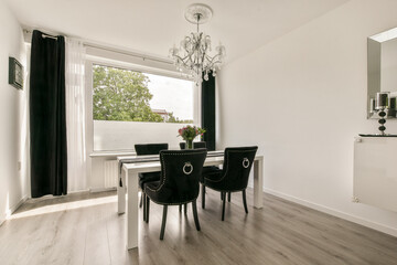 A stylish dining room featuring a modern table, black chairs, large windows, and contemporary decor elements, creating a bright and inviting atmosphere.