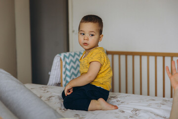 Smiling toddler having fun on bed with blanket. A baby playing hide and seek or peek a boo.