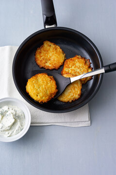 Crispy potato latkes frying in a pan with a side of creamy dip