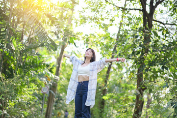 Naklejka premium woman joyfully stretches her arms in lush green forest, basking in sunlight. She wears casual attire, exuding freedom and happiness in nature