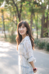 Asian woman enjoying summer day, breathing fresh air in serene park, surrounded by sunlight and greenery, with cheerful expression