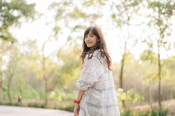 Asian woman enjoying summer outdoors, breathing fresh air in serene park with sunlight filtering...
