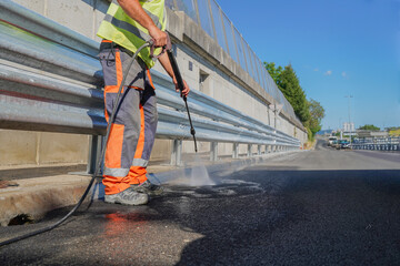 Construction worker using pressure washer to clean road next to aluminum road barriers on highway construction site