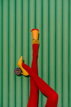 Stylish legs in red tights balancing coffee cup and donut