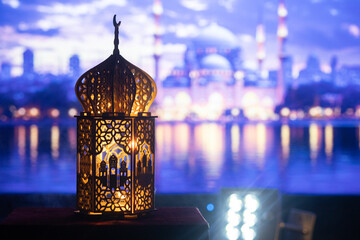 ornamental Arabic lantern with burning candle glowing at night and mosque in background. Festive...