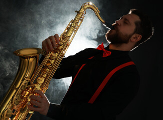 Professional musician playing saxophone on black background with smoke
