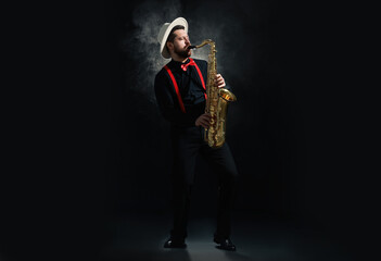 Naklejka premium Professional musician playing saxophone on black background with smoke