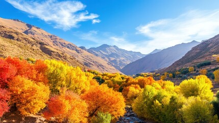 Valley of Colors: A vibrant autumn landscape paints a stunning picture with colorful trees nestled between majestic mountains, under a bright blue sky with fluffy clouds.