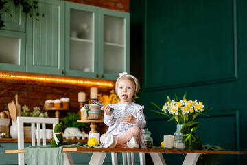  little girl holding a whisk for preparing Easter while sitting on a table at home