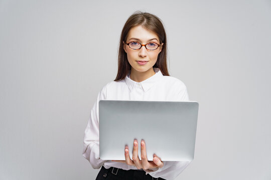 Young woman in white blouse holds laptop while looking confidently at the camera indoors