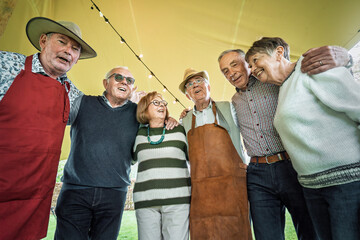 Happy senior friends embracing at outdoor party enjoying friendship