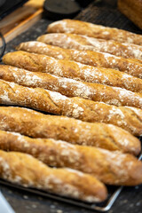 A close-up of multiple freshly baked whole grain baguettes with a golden crust and flour dusting, resting on a cooling rack in a bakery.