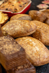 A close-up of various freshly baked artisan bread loaves with a crusty texture, displayed on a cooling rack in a bakery setting.