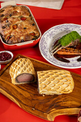 A gourmet beef Wellington with a flaky lattice crust, sliced open to reveal tender beef, served on a wooden board with a holiday feast in the background.