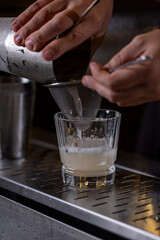A bartender straining a cocktail into a glass using a fine mesh strainer, showcasing professional mixology techniques in a bar setting.