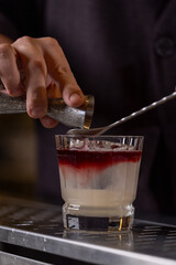 A bartender straining a cocktail into a glass using a fine mesh strainer, showcasing professional...